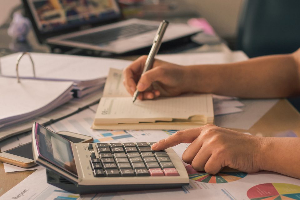 Hands working a desk calculator while writing in a notebook