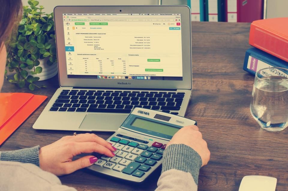 Hands using a calculator next to a laptop showing a spreadsheet